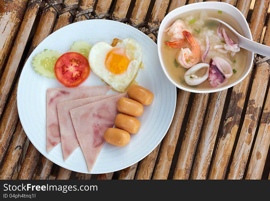 Plate with classic fried egg,ham, sausage and asia soup with seafood breakfast on a bamboo table. Plate with classic fried egg,ham, sausage and asia soup with seafood breakfast on a bamboo table