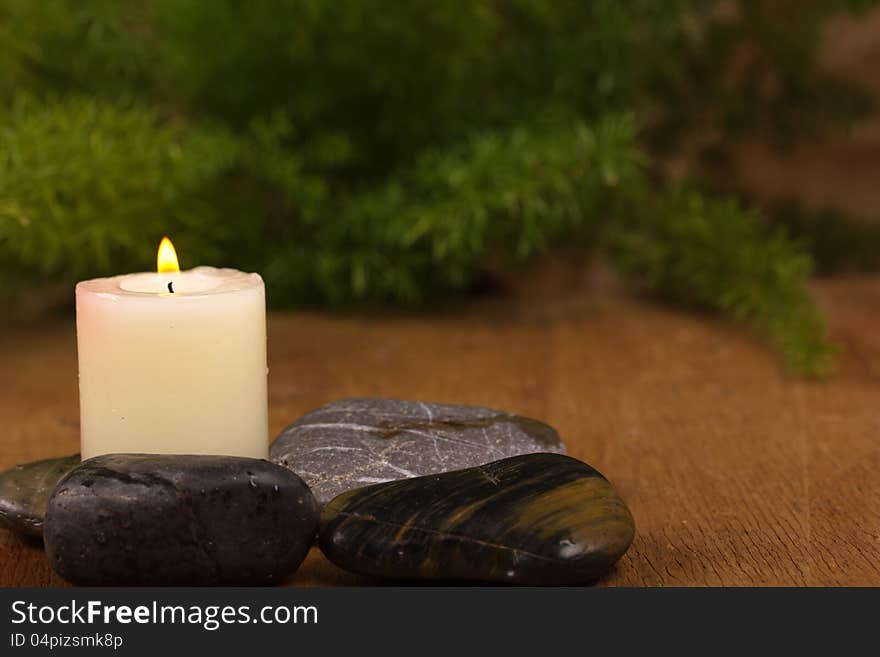 Burning candle and black stones and green leaves on a wooden background. Burning candle and black stones and green leaves on a wooden background