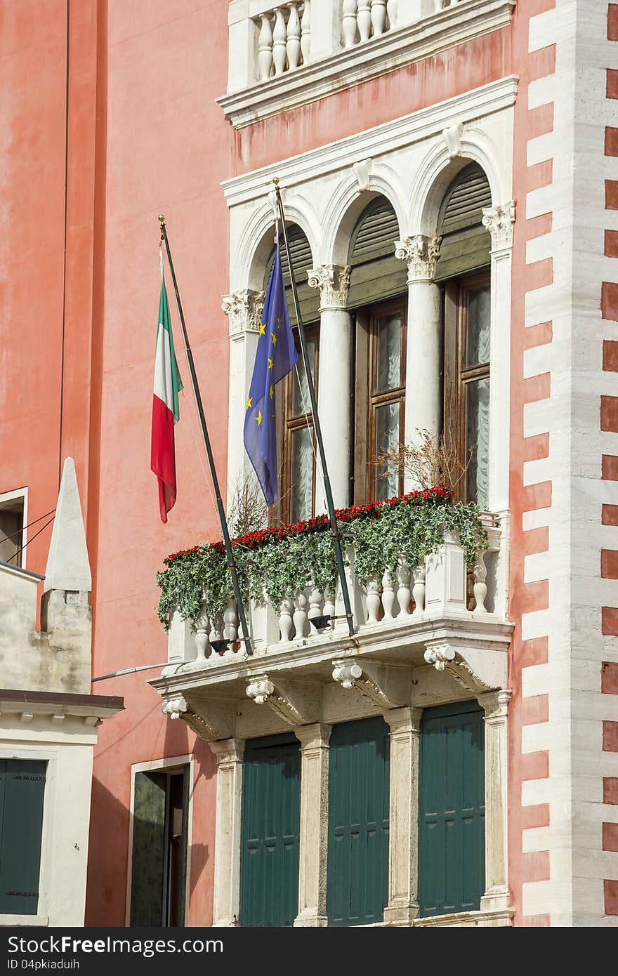 Facade fragment of an ancient building with a balcony, ornaments and flags