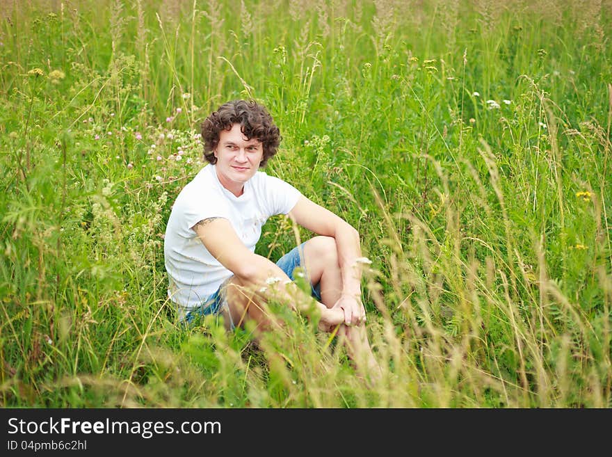 A young man sitting among flowering meadows. A young man sitting among flowering meadows.