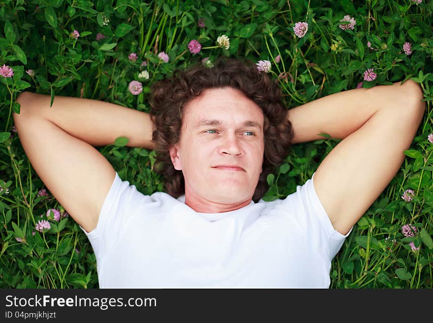 A young man lies on a flowering clover meadow, his hands behind his head. A young man lies on a flowering clover meadow, his hands behind his head.