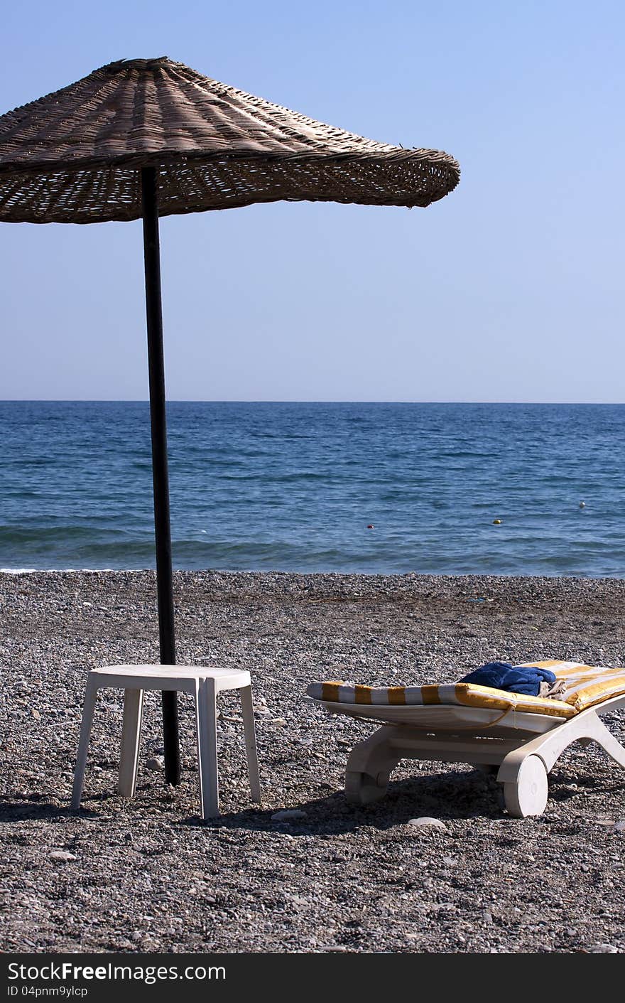 Plastic sun lounger with simple table and a beach umbrella on a deserted beach. Plastic sun lounger with simple table and a beach umbrella on a deserted beach.