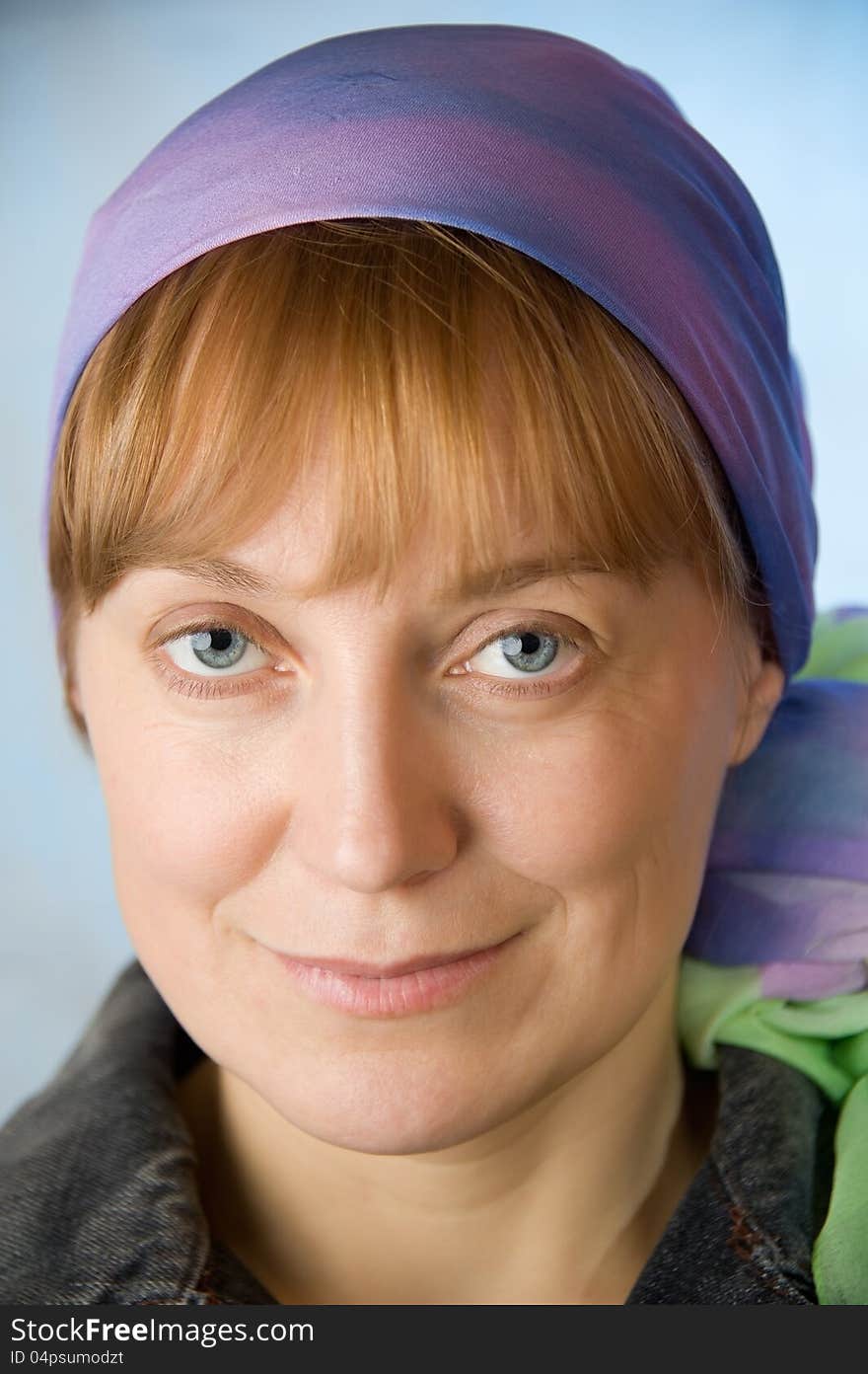 Portrait of adult woman in a bright headscarf. Look at the camera. Blue background. Closeup. Portrait of adult woman in a bright headscarf. Look at the camera. Blue background. Closeup.