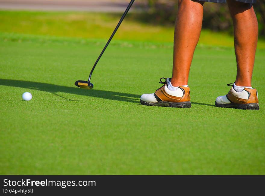 Closeup of golfer putting on the green with the ball in motion and the golfer finishing his swing. Closeup of golfer putting on the green with the ball in motion and the golfer finishing his swing.