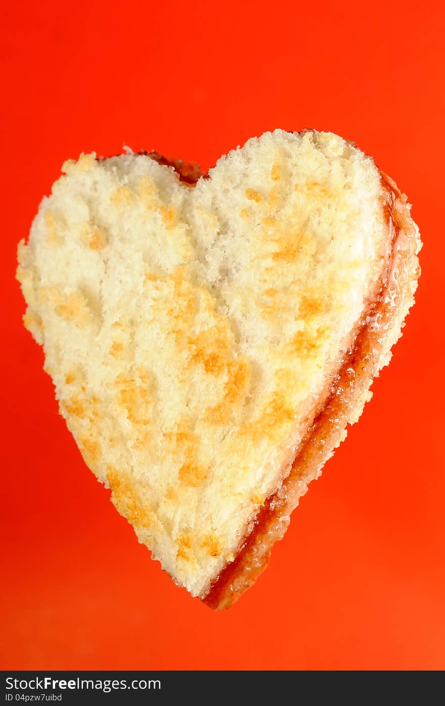 A heart-shaped jam sandwich on a bright red background. A heart-shaped jam sandwich on a bright red background