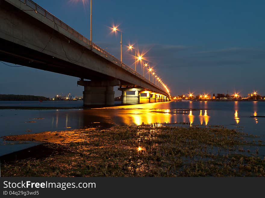 The bridge across the river. View at night. Shining lights on the bridge. The bridge across the river. View at night. Shining lights on the bridge.