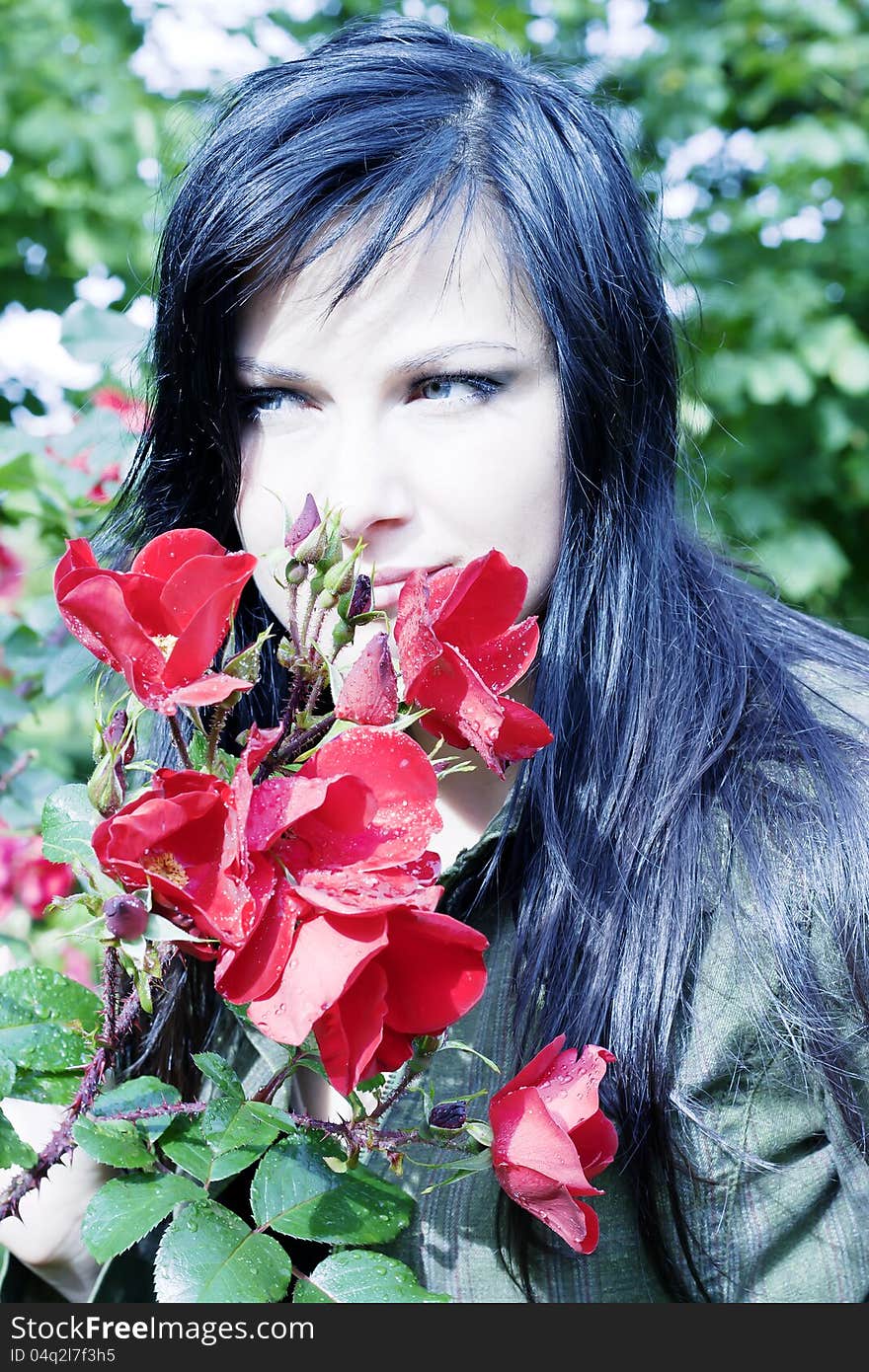 Beautiful brunette near red roses with buds in dew drops