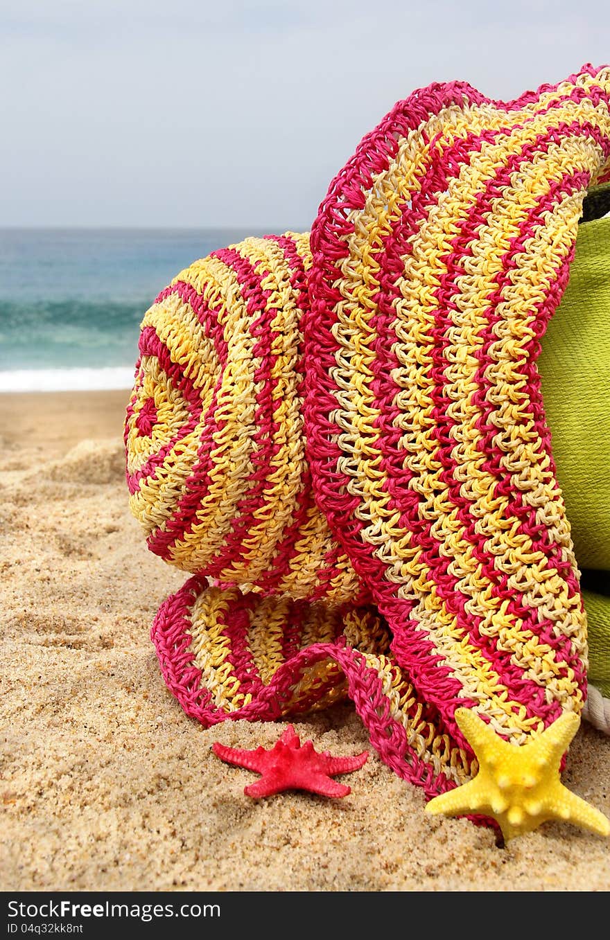 Summer holidays - green beach bag on the seacoast, pink straw hat and funny sea stars. Summer holidays - green beach bag on the seacoast, pink straw hat and funny sea stars