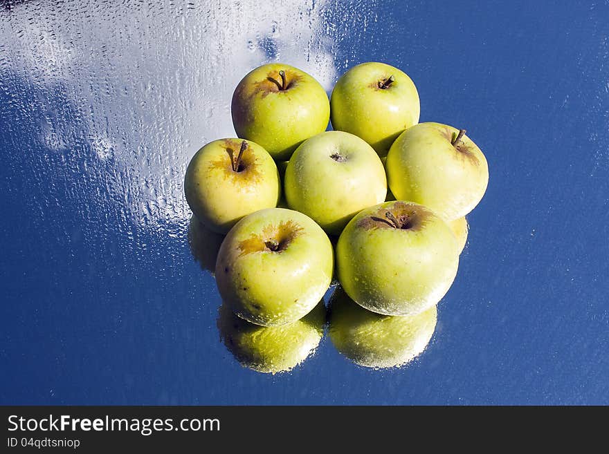 Six yellow apples in flower formation on wet, reflective glass. Six yellow apples in flower formation on wet, reflective glass.