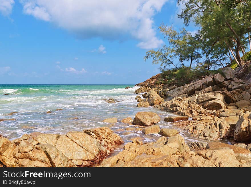 Seascape. The waves of the sea, rocks, trees on the hill and clouds in the sky.