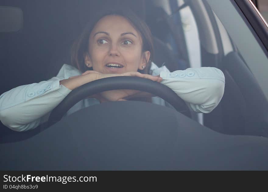 View through the windscreen of a harassed woman waiting in car with her hands and head resting on the steering wheel