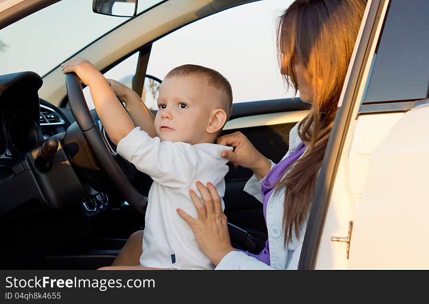 Small boy pretending to drive with his hands on the steering wheel while seated on his mothers lap