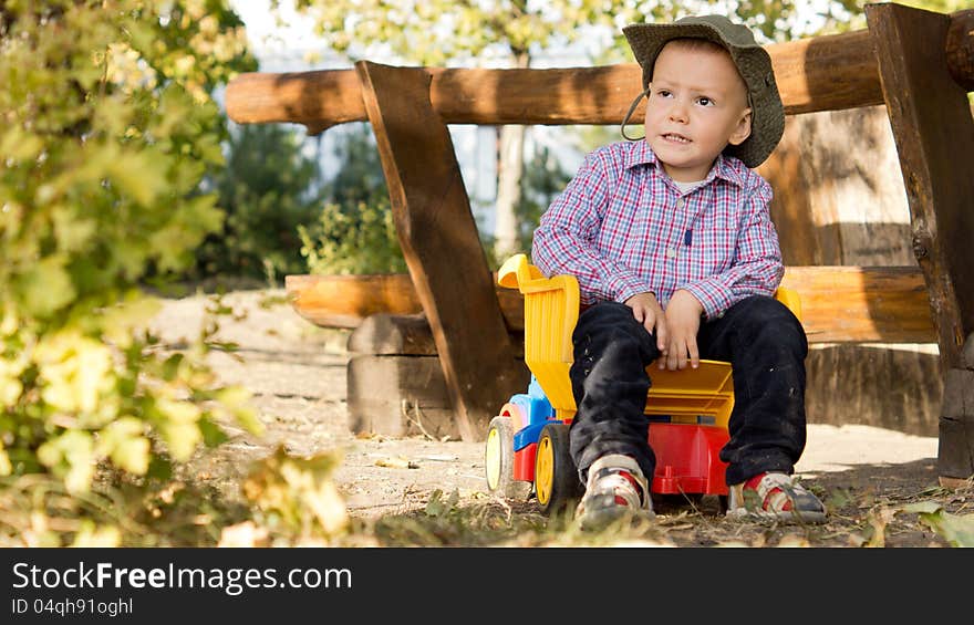 Young boy sitting in the load bed of a toy dump truck alongside a rustic wooden fence in the countryside. Young boy sitting in the load bed of a toy dump truck alongside a rustic wooden fence in the countryside