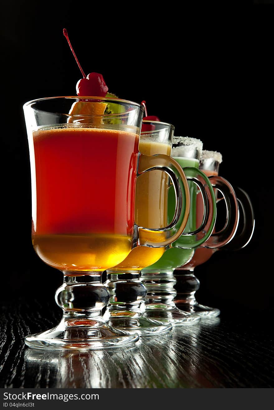 Group of four wine glasses with colored alcoholic cocktails, decorated with fruit and sugar on black bar counter