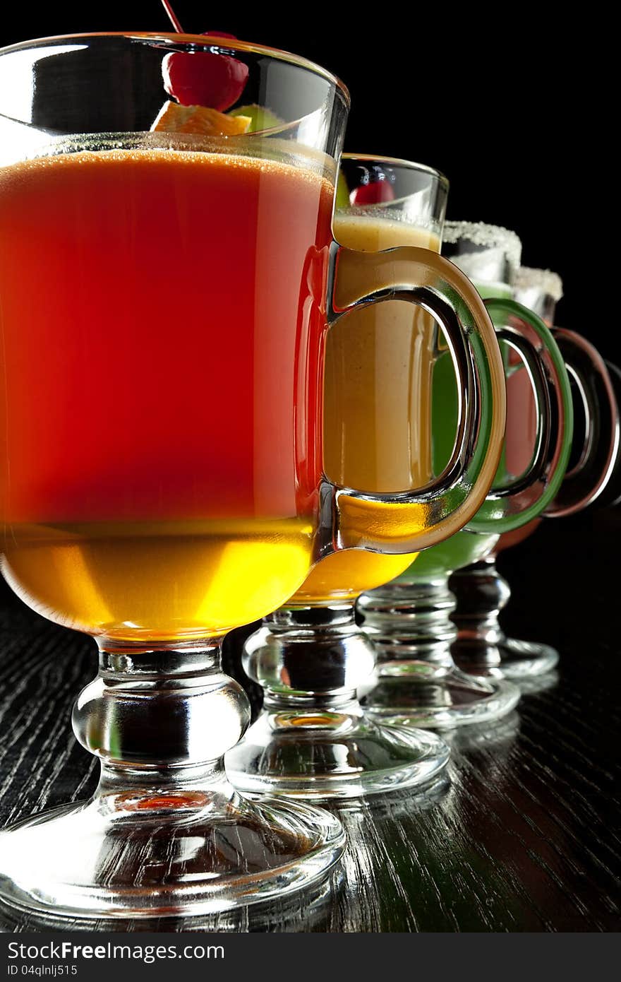 Group of four wine glasses with colored alcoholic cocktails, decorated with fruit and sugar on black bar counter