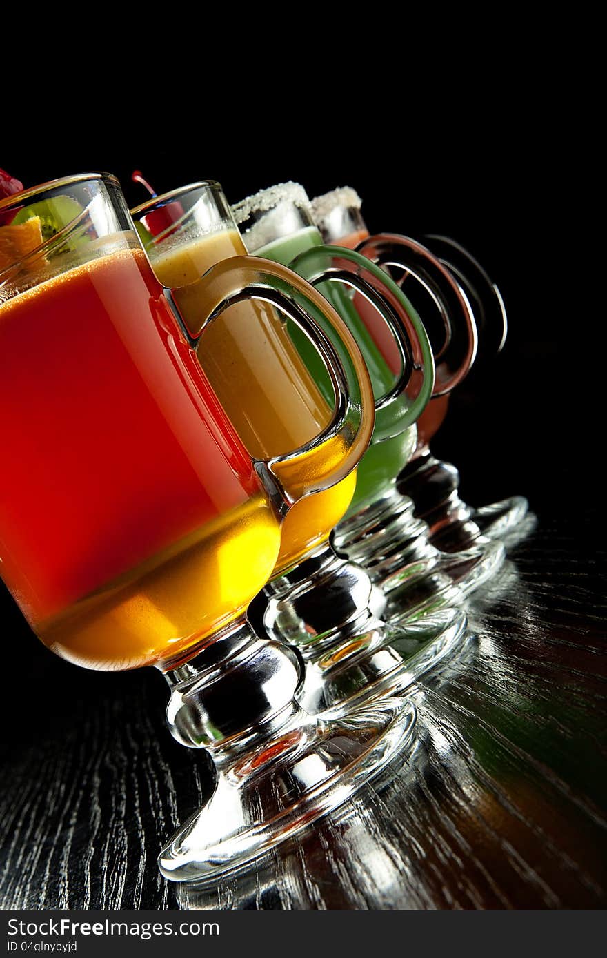 Group of four wine glasses with colored alcoholic cocktails, decorated with fruit and sugar on black bar counter