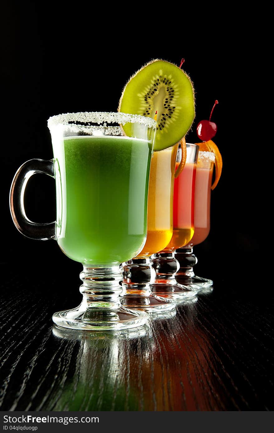 Group of four wine glasses with colored alcoholic cocktails, decorated with fruit and sugar on black bar counter