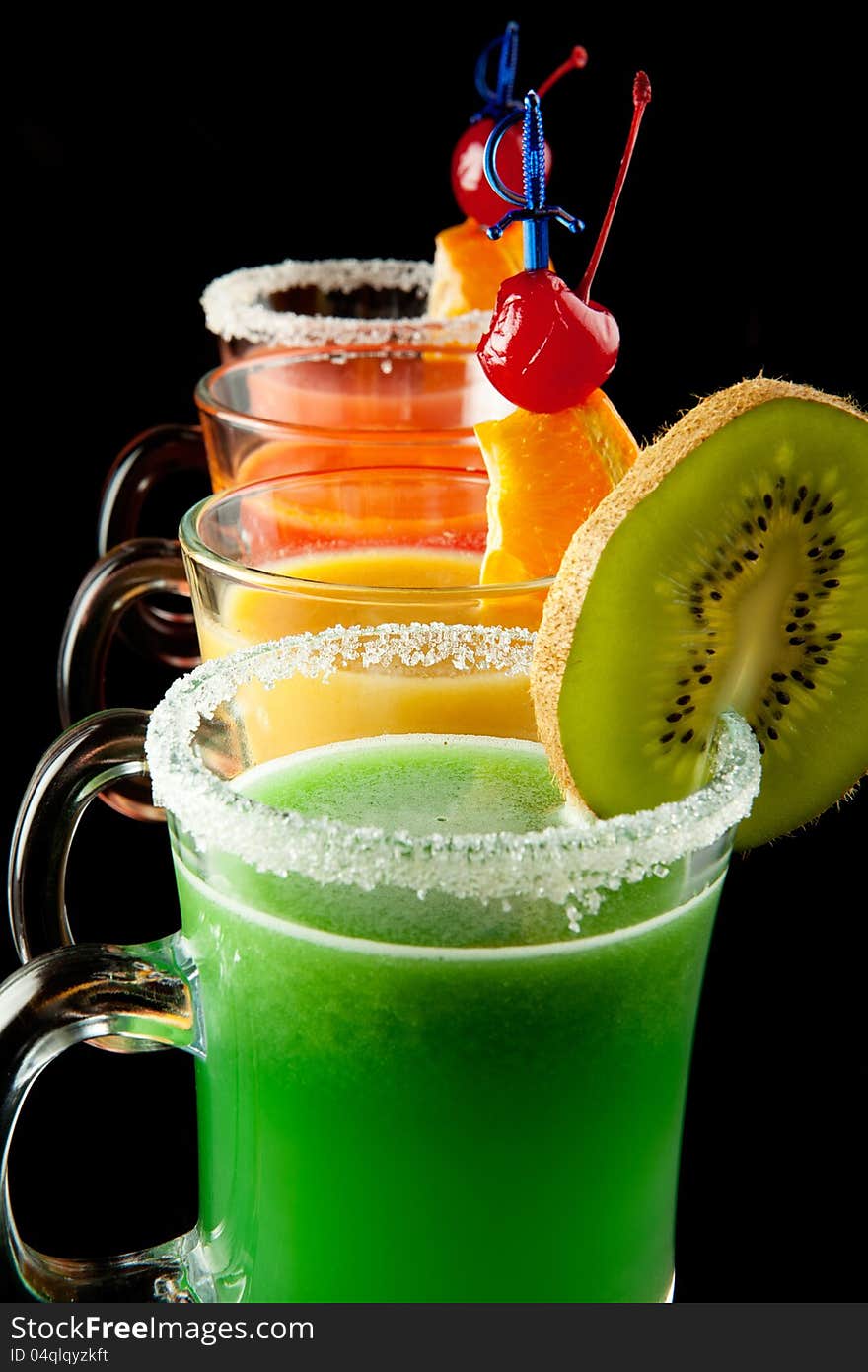 Group of four wine glasses with colored alcoholic cocktails, decorated with fruit and sugar on black bar counter