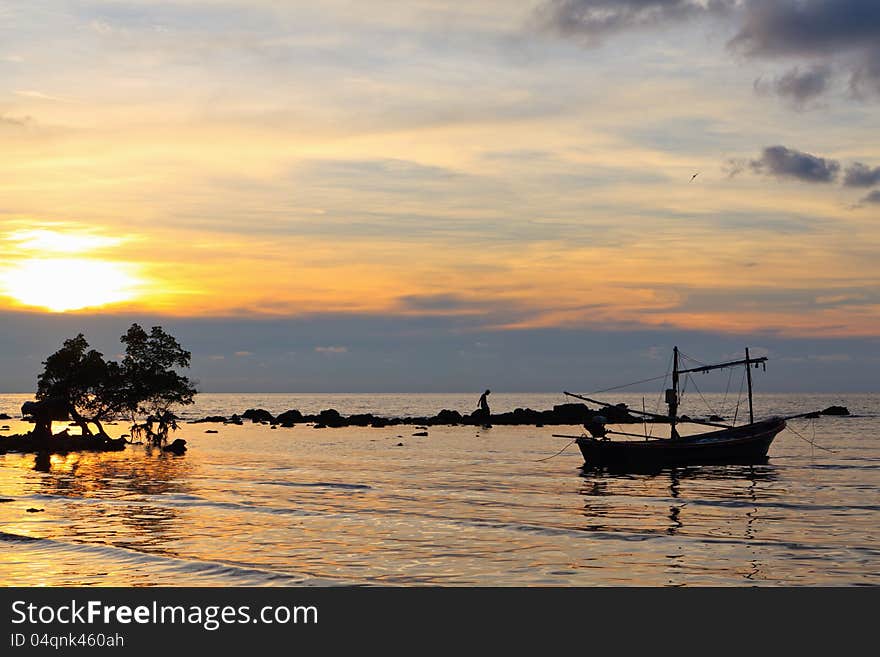 A small fishing boat and a tree in the sea at sunset. A small fishing boat and a tree in the sea at sunset.