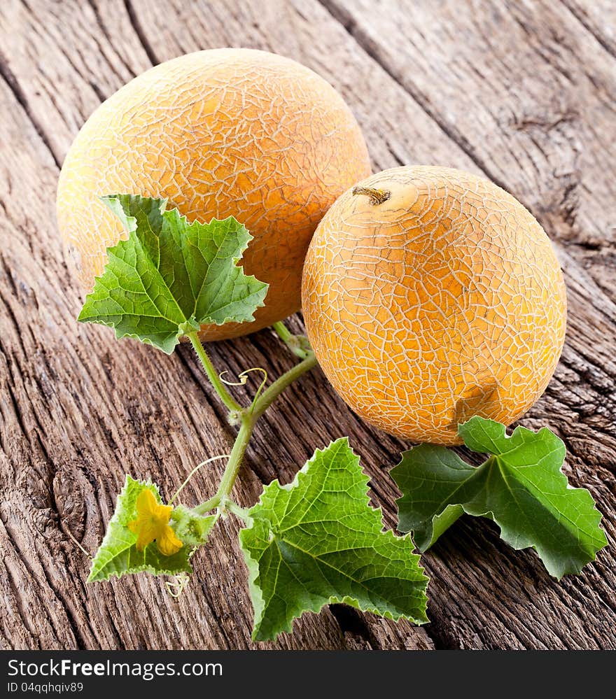 Two melons with the leaves on the old wooden table.