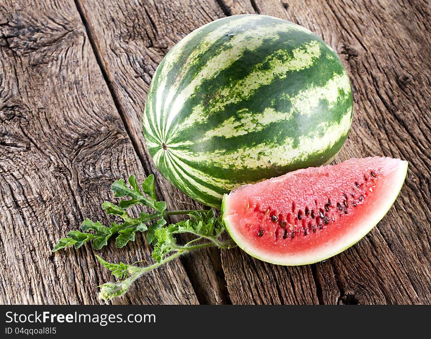 Watermelon with a slice and leaves on a old wooden table.