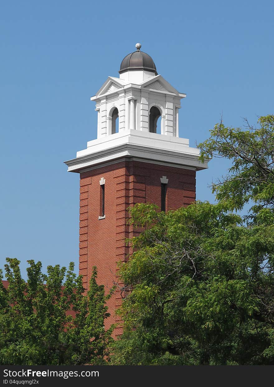 Close-up of a red brick tower with a white top and dome, with trees and a blue sky. Close-up of a red brick tower with a white top and dome, with trees and a blue sky.