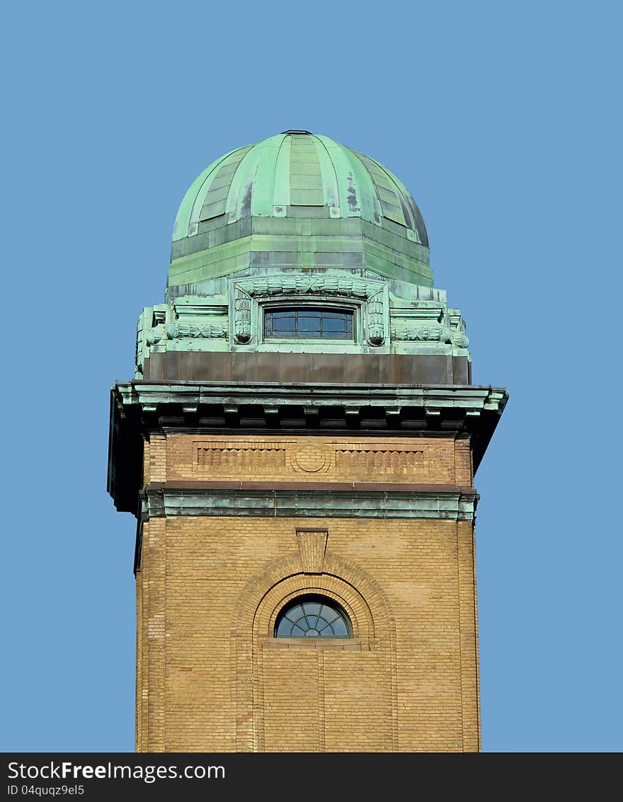 Green weathered copper dome or cupola, with a window, on top of an old brick tower. Isolated against a blue sky. Green weathered copper dome or cupola, with a window, on top of an old brick tower. Isolated against a blue sky.