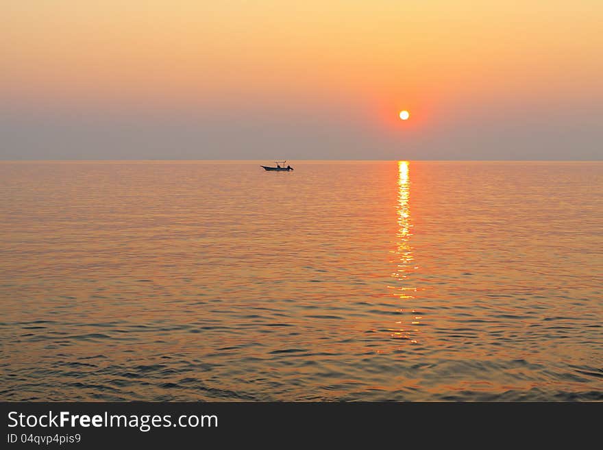 A small fishing boat in the sea at sunset.