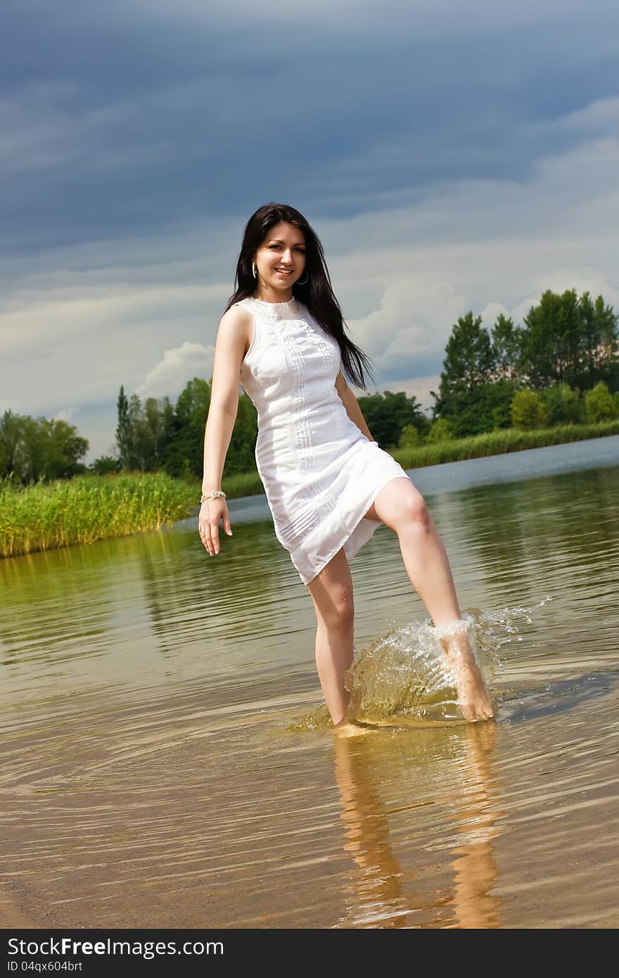 Young woman makes fun on the lake doing splashes of water