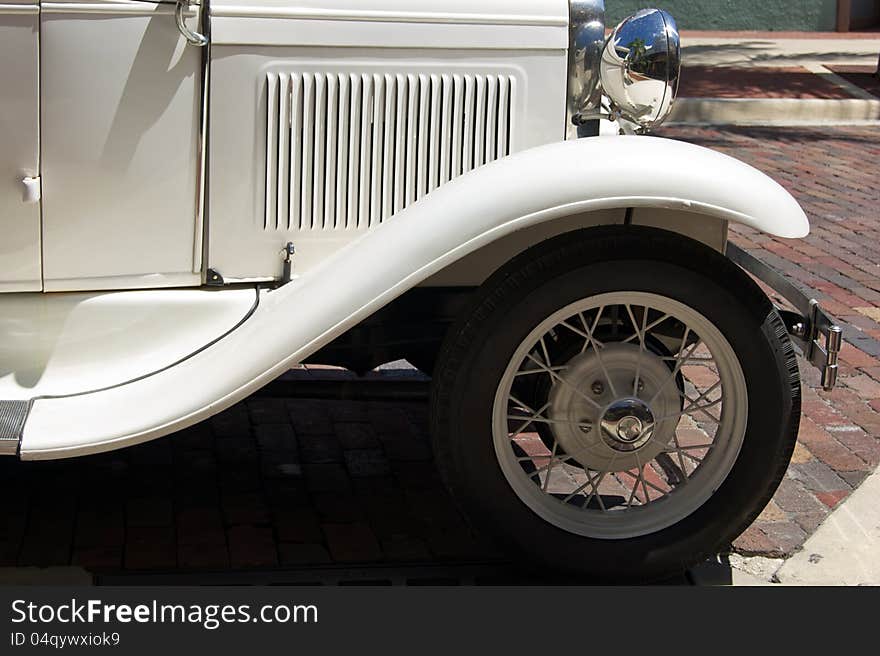 Side view of old antique automobile, showing hood vents, fender and headlights on brick road. Side view of old antique automobile, showing hood vents, fender and headlights on brick road