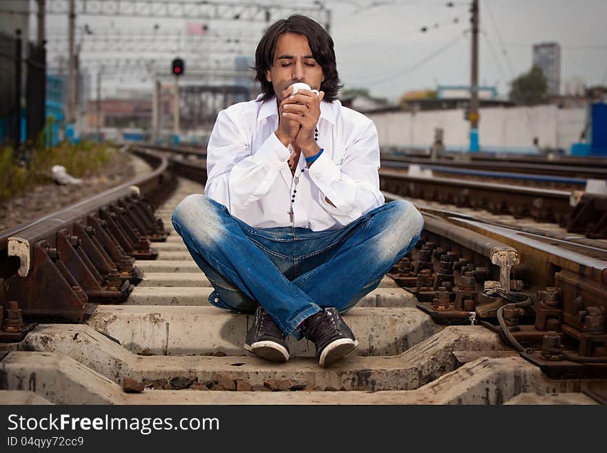 Man is sitting on the rails and drinking coffee. Man is sitting on the rails and drinking coffee