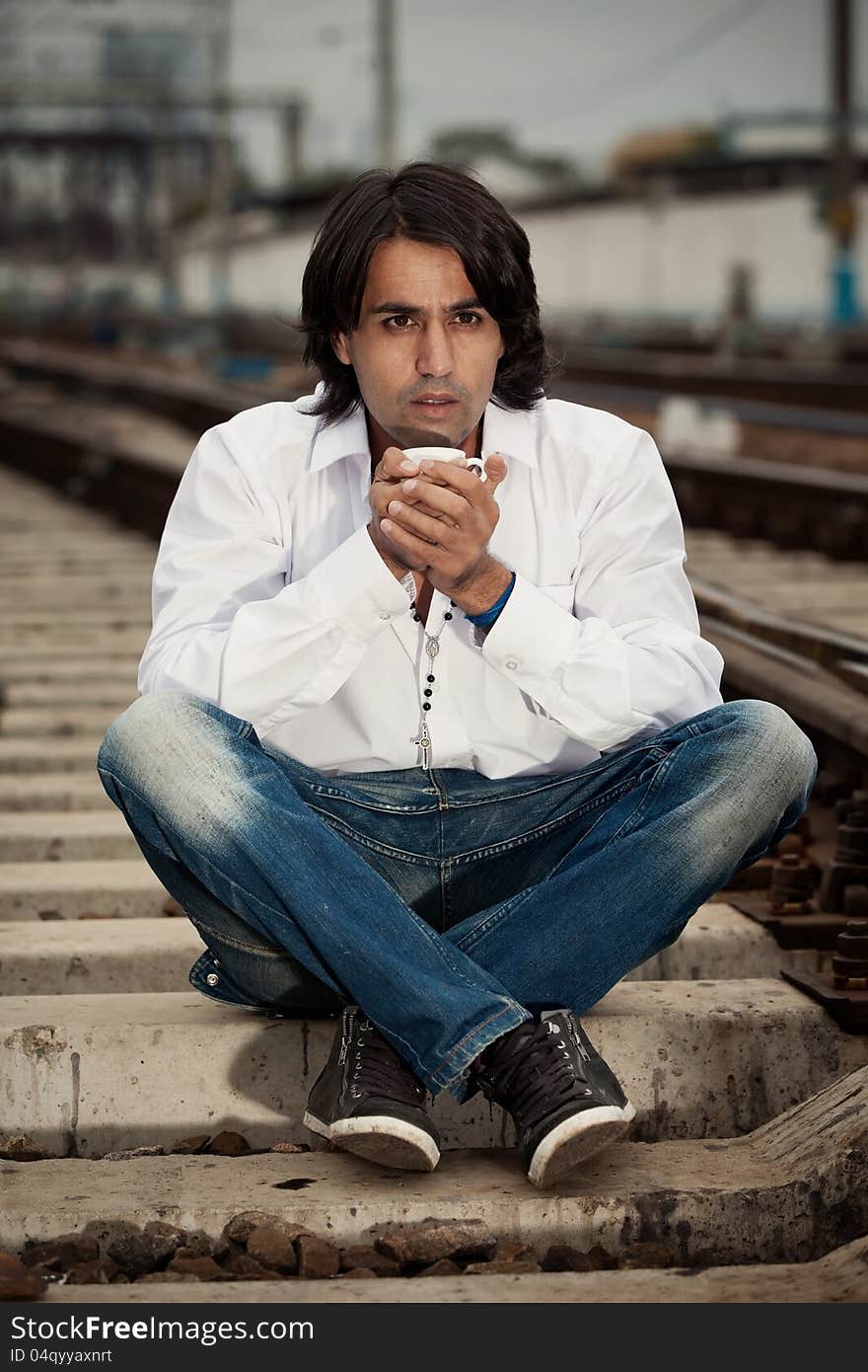 Man is sitting on the rails and drinking coffee. Man is sitting on the rails and drinking coffee