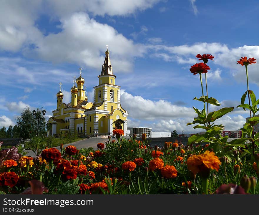 Nadym. The Orthodox temple with flowerses on background blue sky. Nadym. The Orthodox temple with flowerses on background blue sky.