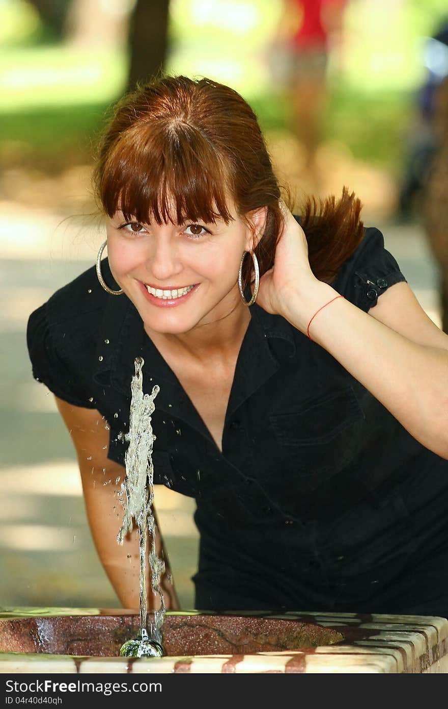 Woman drinking water from a street tap outdoor in a park