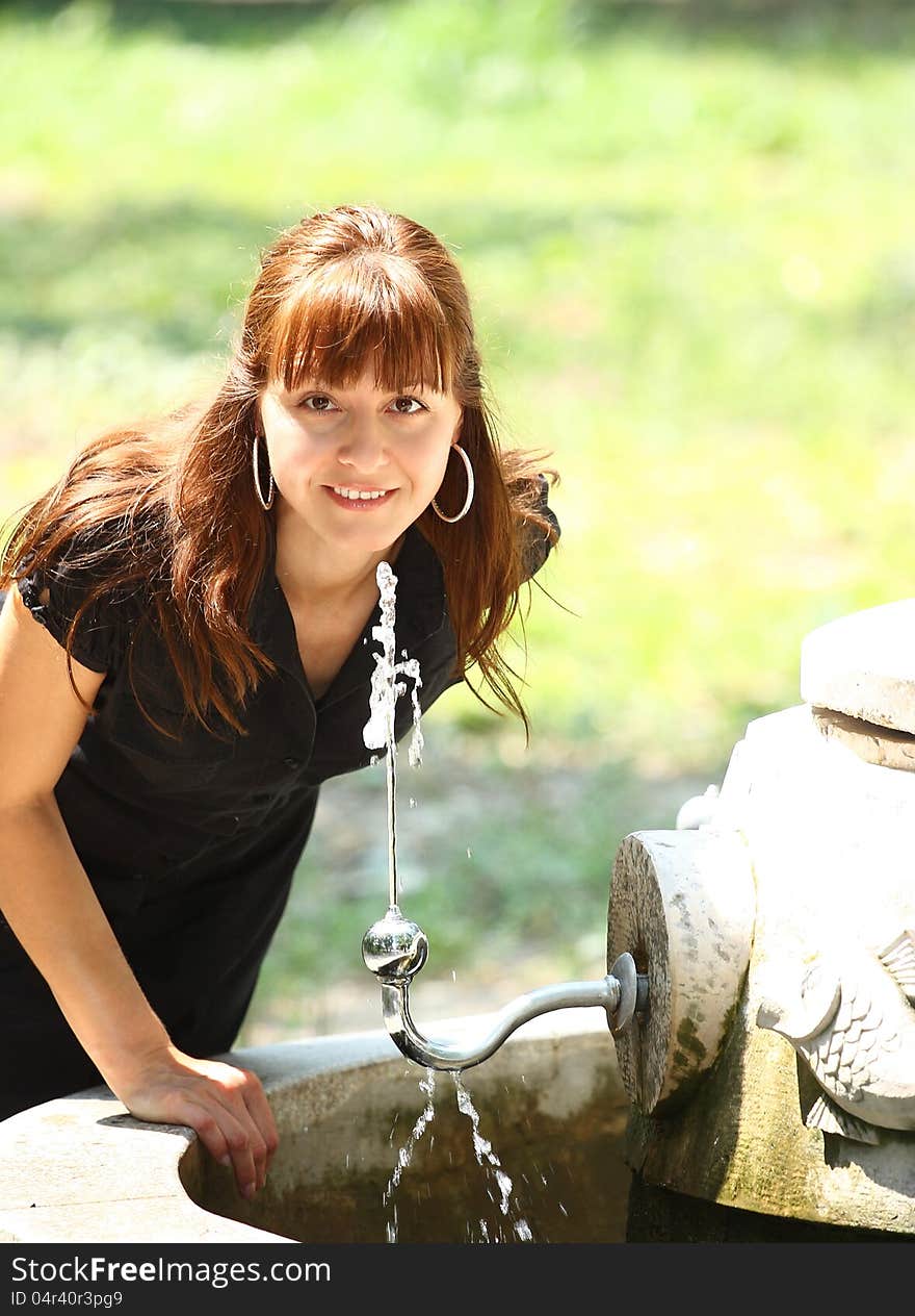 Woman drinking water from a tap outdoor in a park. Woman drinking water from a tap outdoor in a park