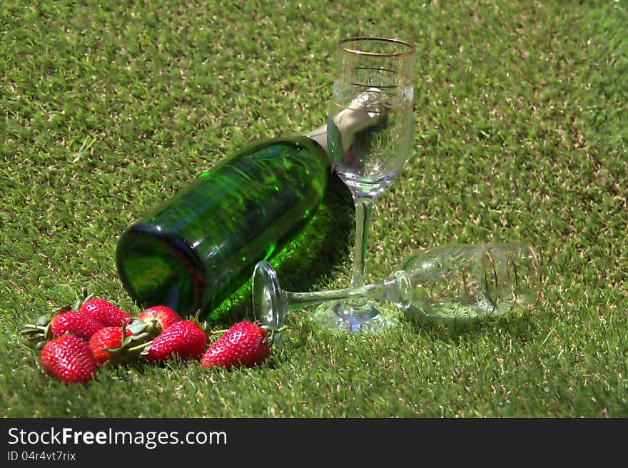 Champagne bottle, glasses and strawberries on the green grass