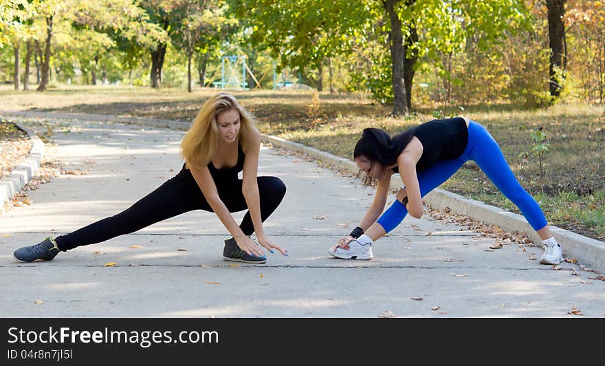 Two fit young women athletes working out together doing stretching exercises in a park in a health and fitness concept. Two fit young women athletes working out together doing stretching exercises in a park in a health and fitness concept