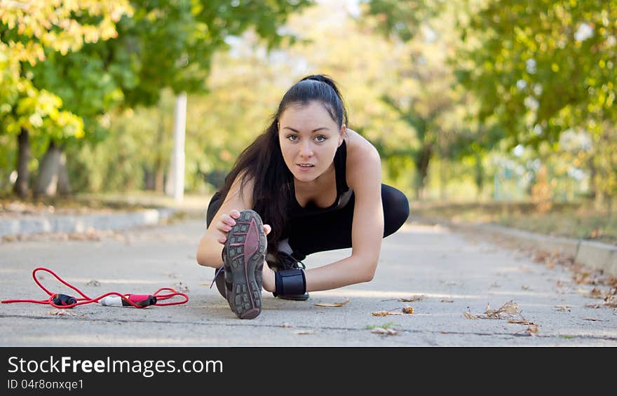 Low angle view of a young attractive woman athlete stretching with her leg extended close to the road surface as she warms up for her workout and training. Low angle view of a young attractive woman athlete stretching with her leg extended close to the road surface as she warms up for her workout and training