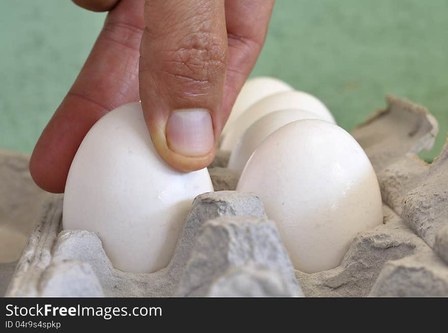 Closeup of fingers of man grabbing an egg from carton. Closeup of fingers of man grabbing an egg from carton