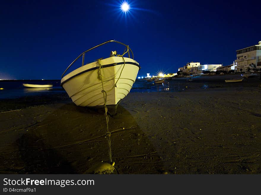 Close view of a white and blue traditional fishing boat anchored on a beach at night.