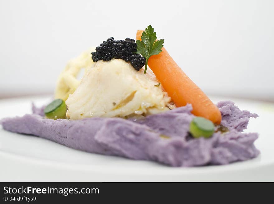 Top view of a beautiful gourmet dish of cod fish, mashed potato, carrot and other delicious ingredients.