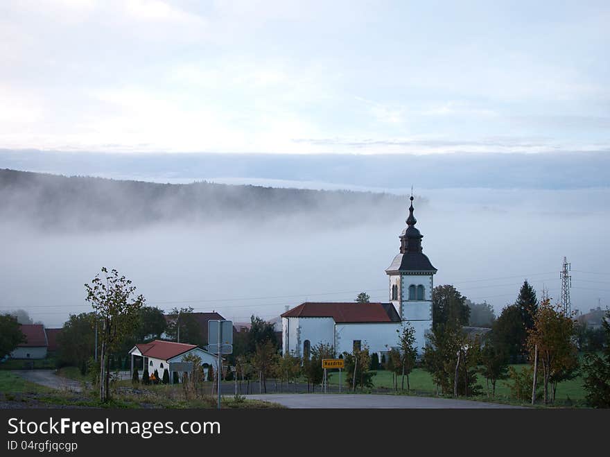 Morning village with church and fog in background.