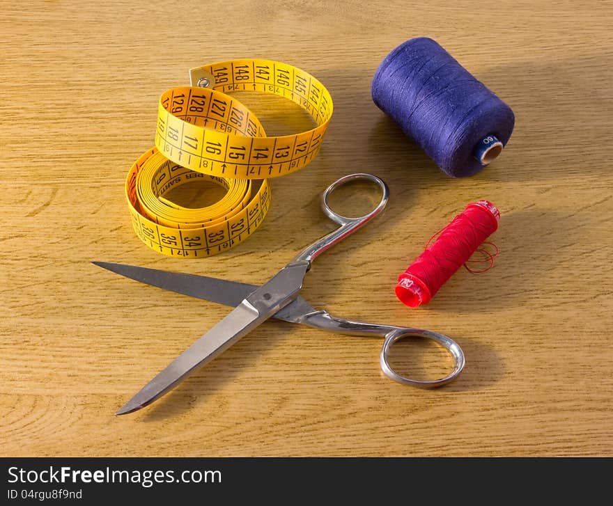 Spools, scissors and a measuring tape on a wooden counter. Spools, scissors and a measuring tape on a wooden counter