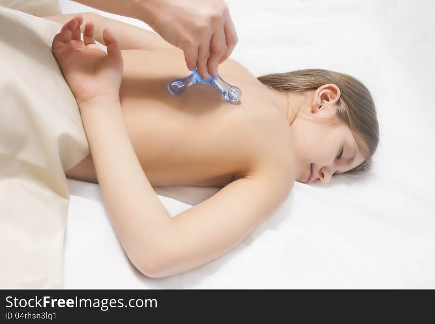 Little young caucasian girl is beeing treated with a massage lying on white linen downwards. Little young caucasian girl is beeing treated with a massage lying on white linen downwards