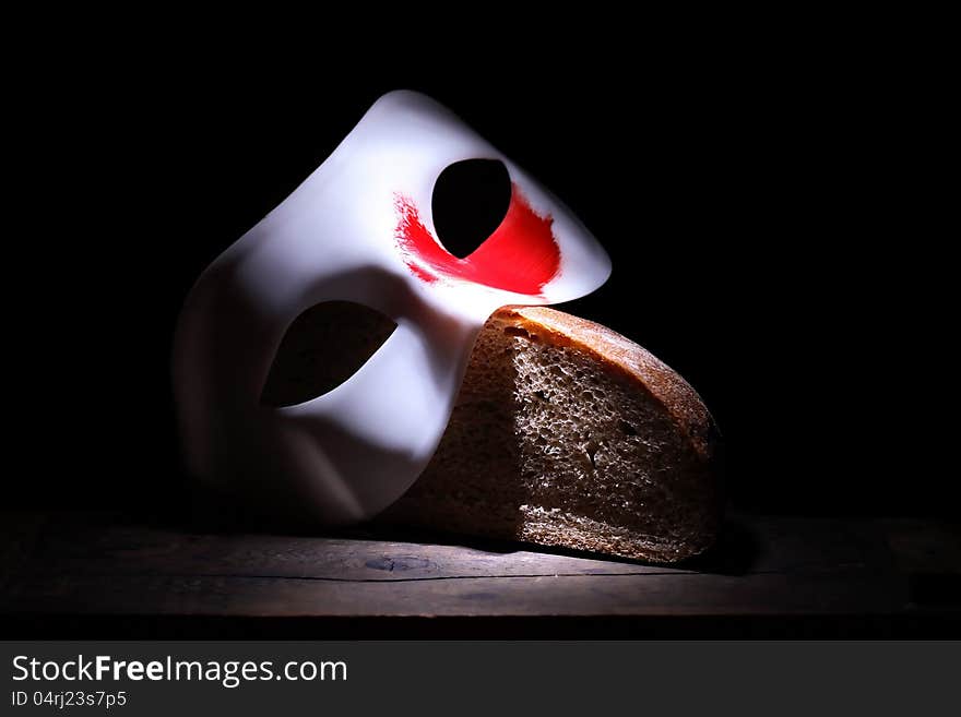 Roman Empire concept. White mask with red spot lying on bread on black background. Roman Empire concept. White mask with red spot lying on bread on black background