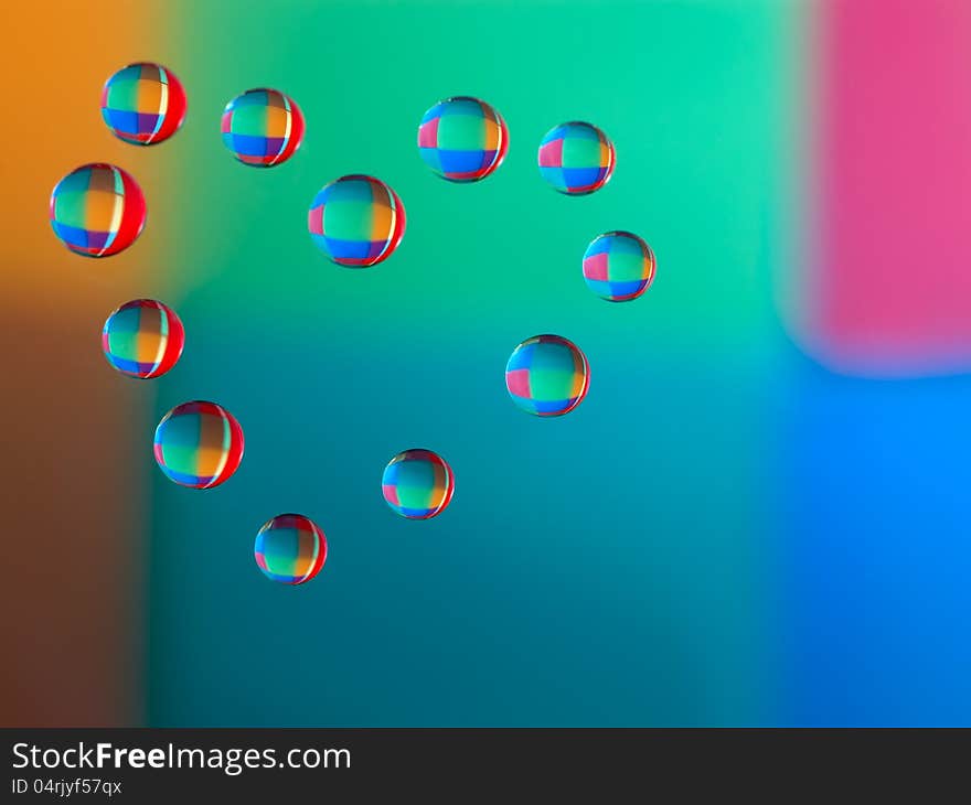 Drops of water on glass in a heart shaped. Colorful background is reflected in the drops. macro. Drops of water on glass in a heart shaped. Colorful background is reflected in the drops. macro