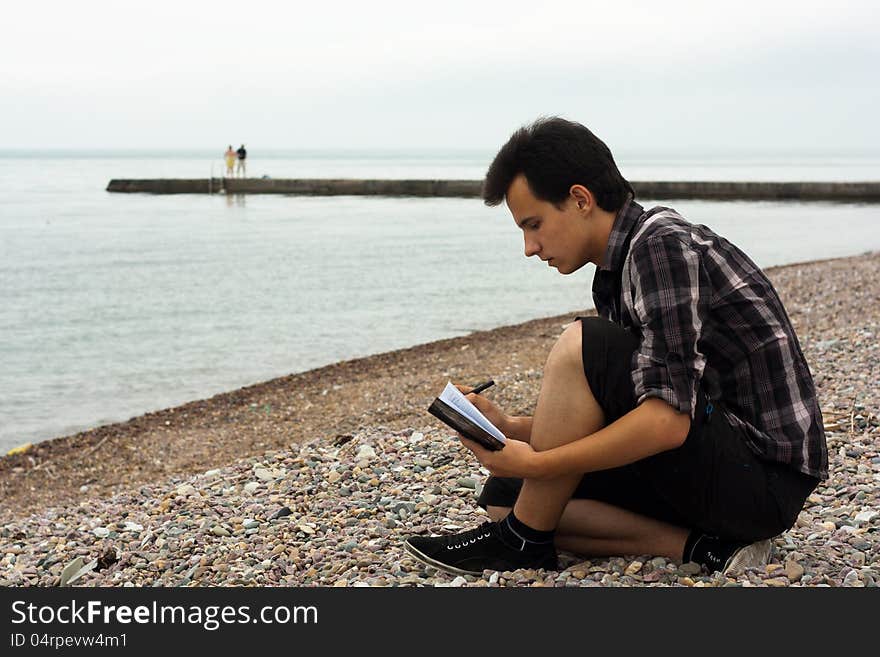 Boy sit on the sea stones and write in notebook. Boy sit on the sea stones and write in notebook