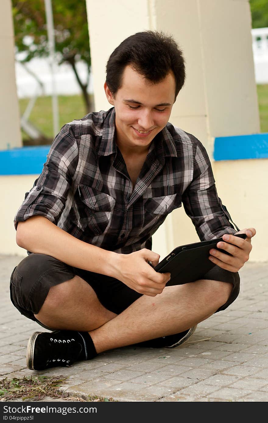 Young man sit on the sidewalk and work on the flatbed computer. Young man sit on the sidewalk and work on the flatbed computer