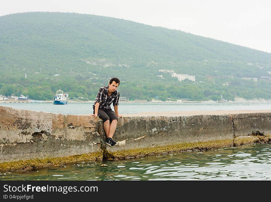 Sad young man sits on sea wall