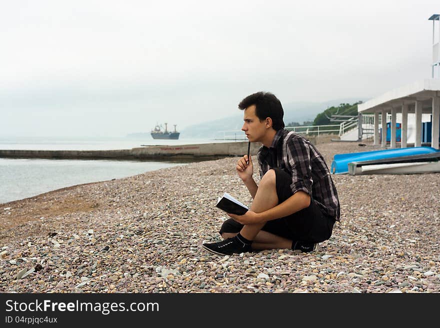 Boy sit on the sea stones and write in notebook. Boy sit on the sea stones and write in notebook